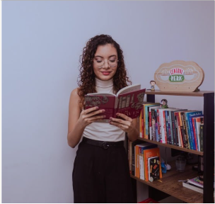 Ruth lendo um livro ao lado de sua estante